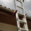 Een close-up van de RMBO® Ladder Klem die een uitschuifbare ladder vastmaakt aan de rand van een pannendak onder een bewolkte hemel.