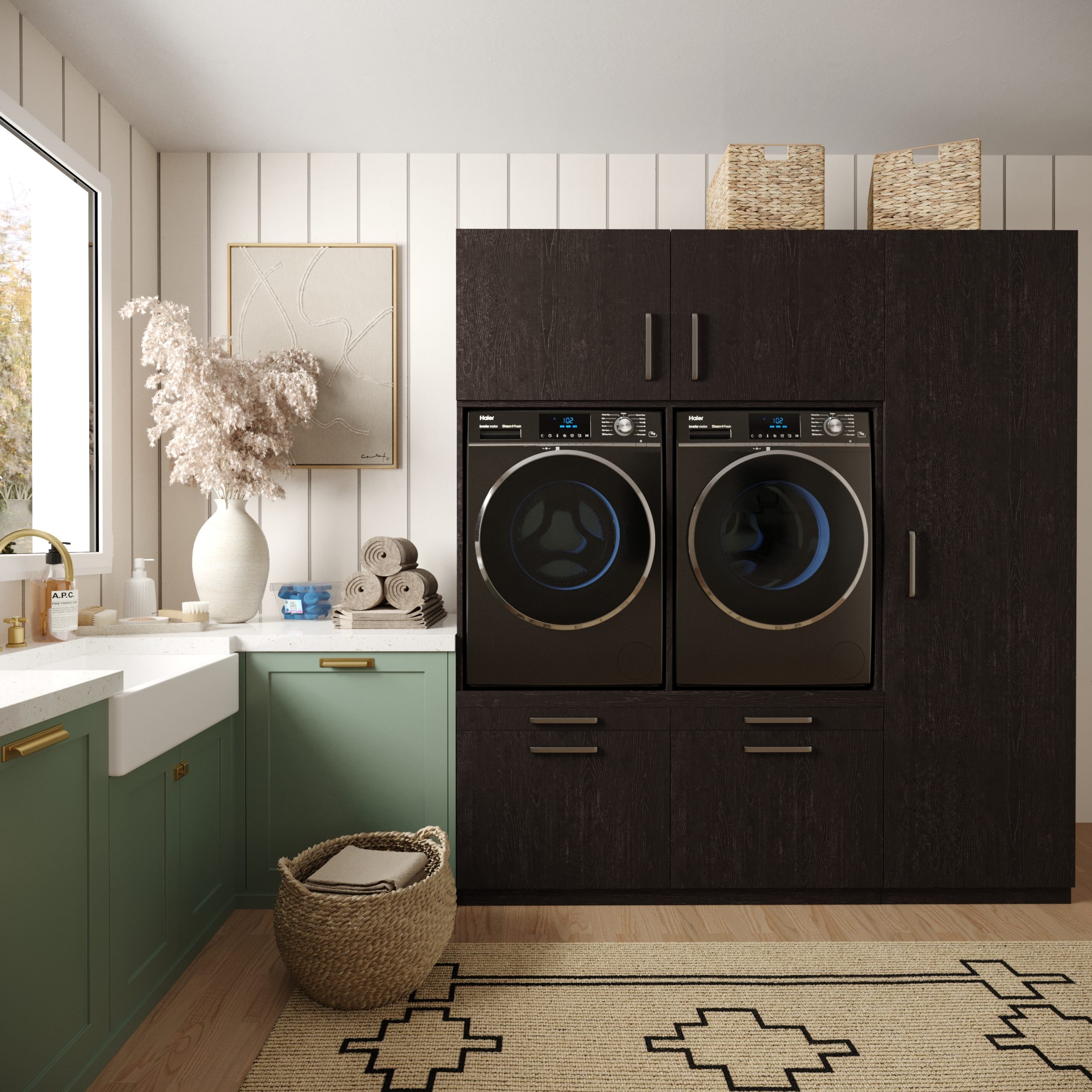 Moderne wasruimte met groene onderkasten, een wit aanrechtblad en gestapelde donkerhouten kasten met daarin een wasmachine en droger met voorlader. Een mand, opgerolde handdoeken en decoratie geven de ruimte warmte. Licht schijnt door een groot raam.