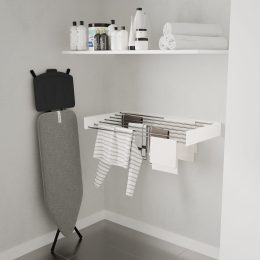Een minimalistische wasruimte met een opvouwbare strijkplank, een droogrek aan de muur met gestreepte kleding en een plank erboven met wasbenodigdheden en netjes opgerolde handdoeken.