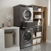 Moderne wasruimte met een wasmachine en droger boven elkaar, voorzien van het Tussenstuk wasmachine & droger XL Zwart – Universeel voor extra stabiliteit en gebruiksgemak, zwarte manden, houten planken voor flessen en wasbenodigdheden, een wasmand en decoratieve bloemen op het aanrecht. Zwart-witte geometrische vloertegels versterken de eigentijdse uitstraling.