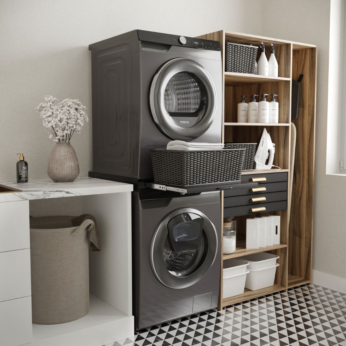 Moderne wasruimte met een wasmachine en droger boven elkaar, voorzien van het Tussenstuk wasmachine & droger XL Zwart – Universeel voor extra stabiliteit en gebruiksgemak, zwarte manden, houten planken voor flessen en wasbenodigdheden, een wasmand en decoratieve bloemen op het aanrecht. Zwart-witte geometrische vloertegels versterken de eigentijdse uitstraling.