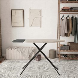 In een stijlvolle, opgeruimde kamer met een neutrale inrichting staat een strijkplank, met op de achtergrond twee abstracte kunstwerken aan de muur, opgehangen kleding en opbergplanken.